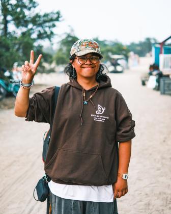 Ivan holding a peace sign in front of a sandy background on the Folk On The Rocks site.